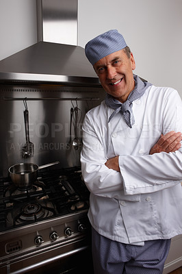Smiling senior chef with hands folded standing by gas stove