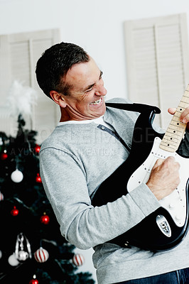 Mature man playing guitar with Christmas tree in background